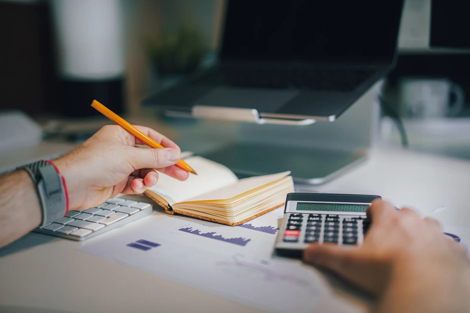 Revisión a mano de cuotas de amortización con calculadora, cuaderno y gráficos impresos, antes de cuadrar la tabla fiscal y la contable