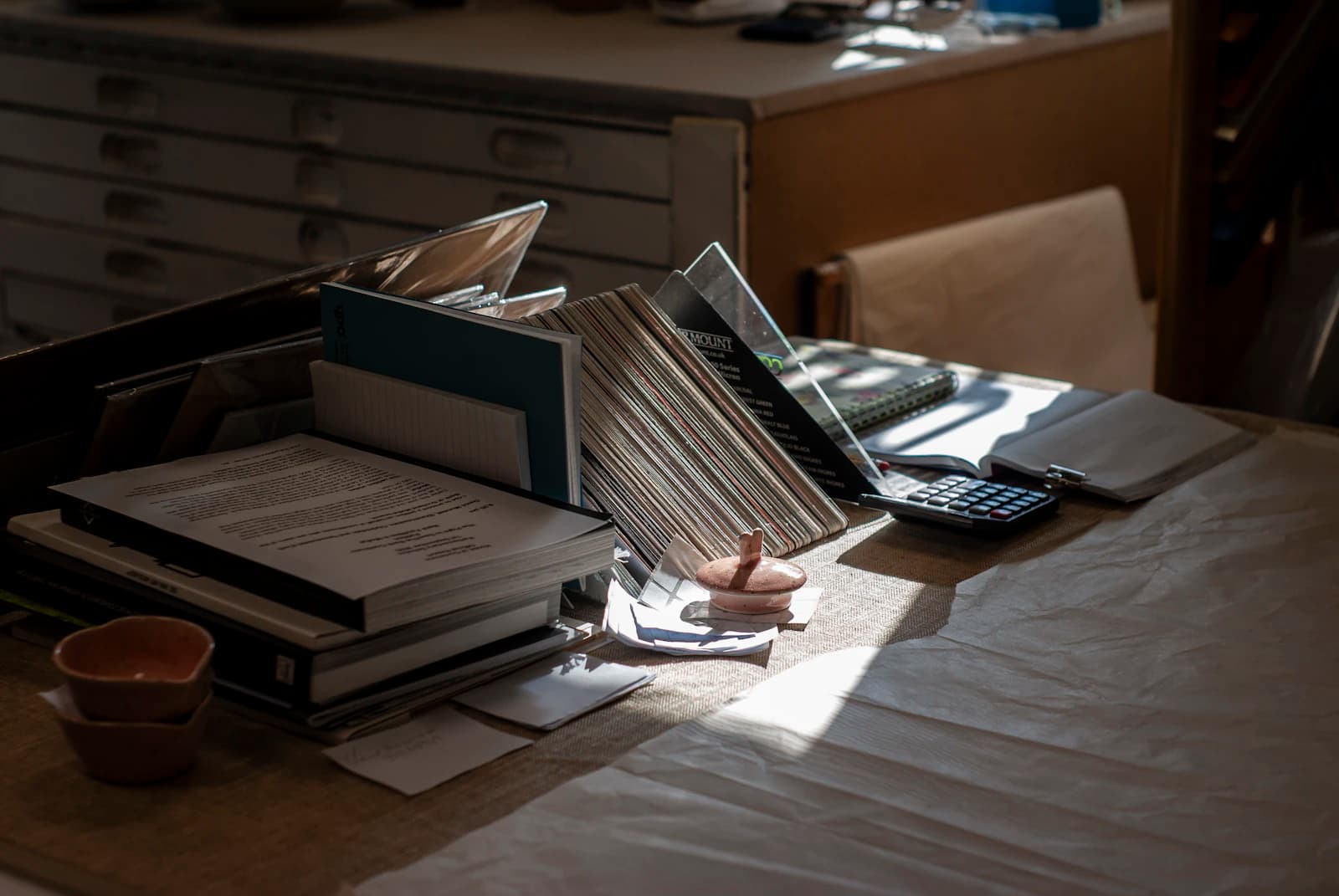 Escritorio con libros, papeles y calculadora bajo la luz de la ventana, donde se calcula el coste de salir de A3