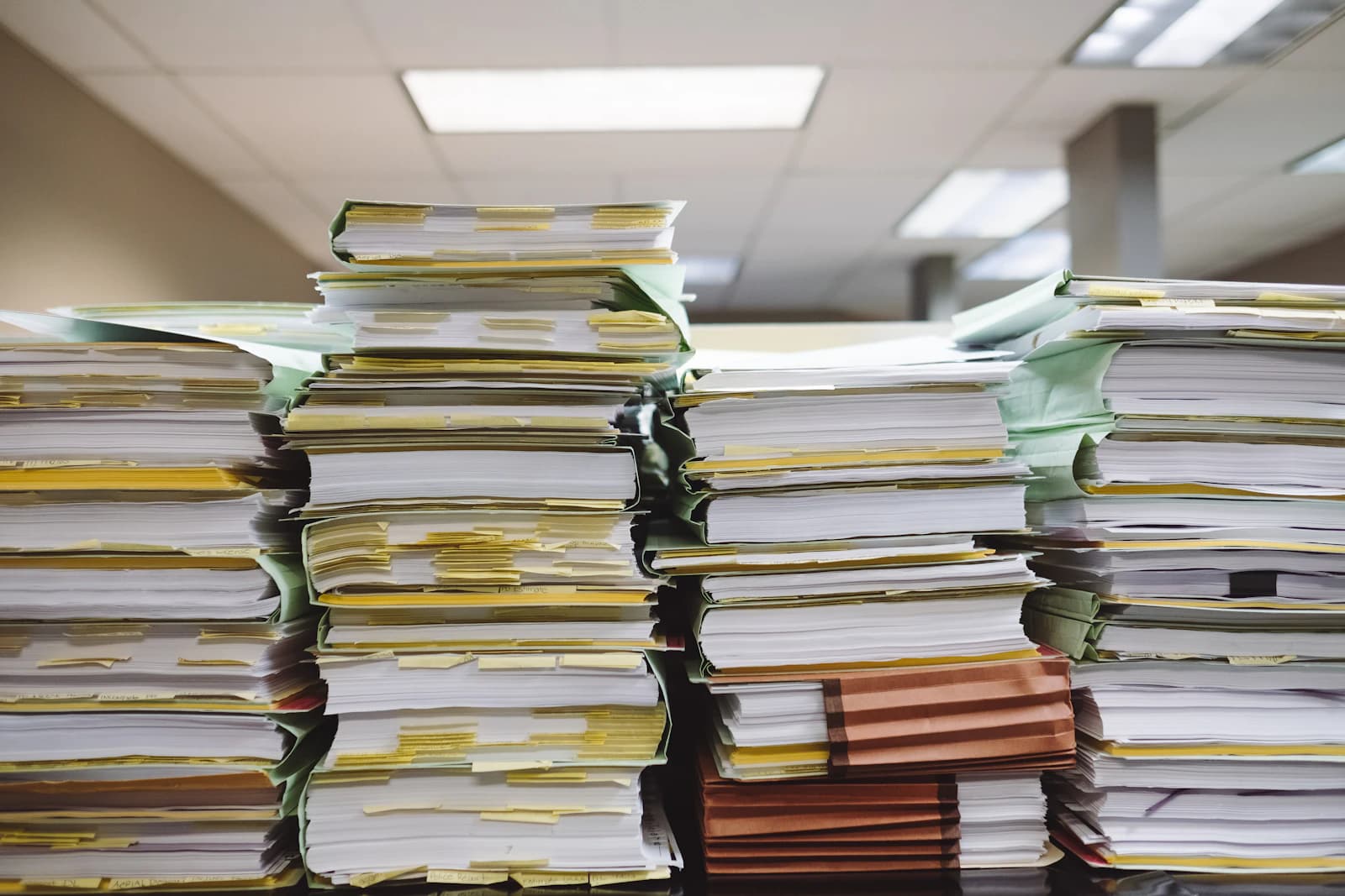 Pilas de carpetas y expedientes en papel sobre una mesa de oficina, la suite de Contasol, Factusol y Nominasol por separado