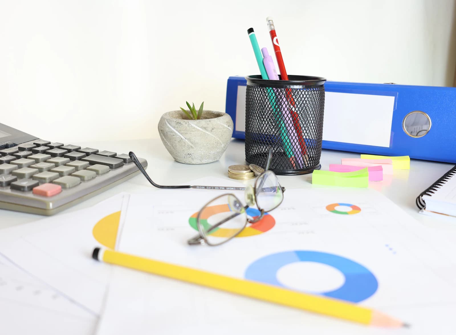 Escritorio con calculadora, gafas, gráficos impresos y archivador, para responder la pregunta del precio de partida de ERPNext