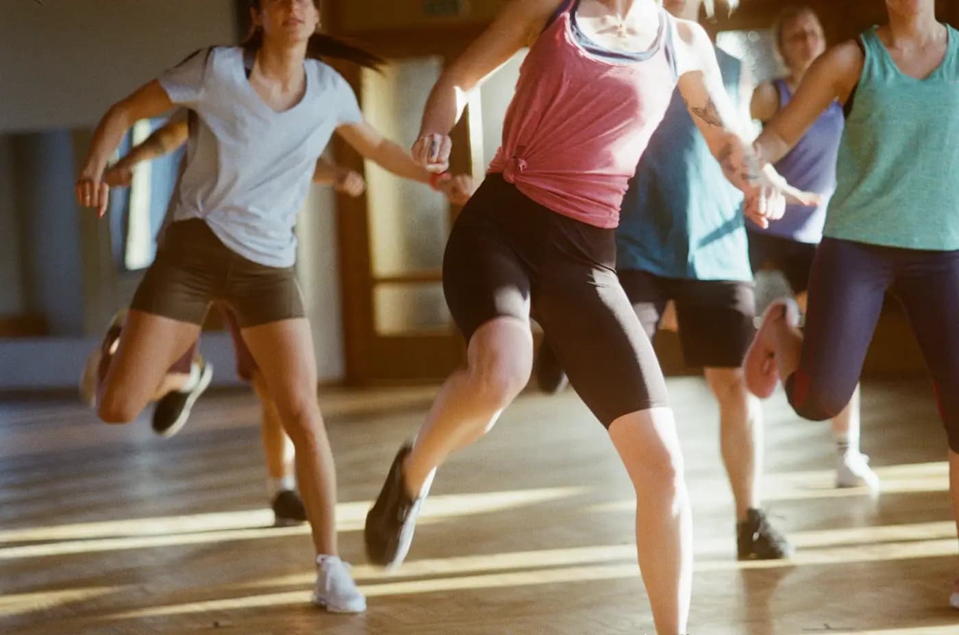 Clase colectiva en la sala de un gimnasio, con varias socias haciendo ejercicio sobre suelo de madera con luz cálida
