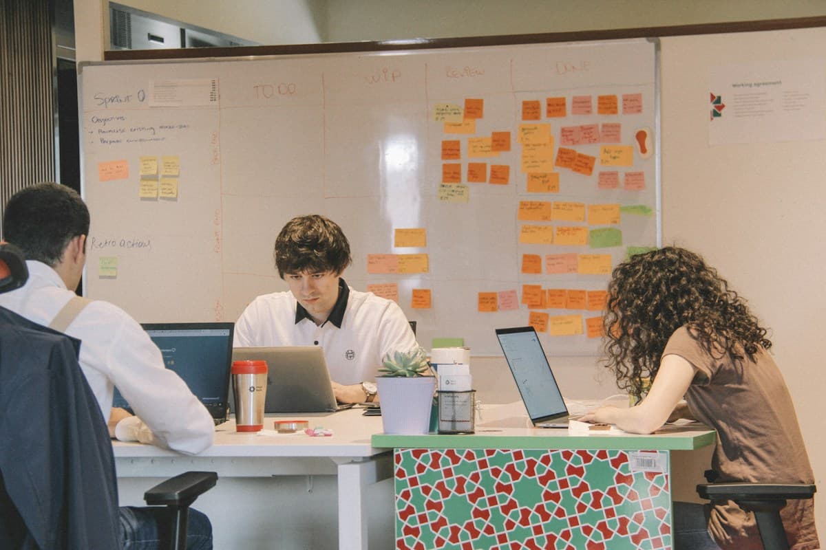 Equipo trabajando con portátiles delante de un tablero de tareas con notas adhesivas, un mismo equipo para cada servicio ERPNext