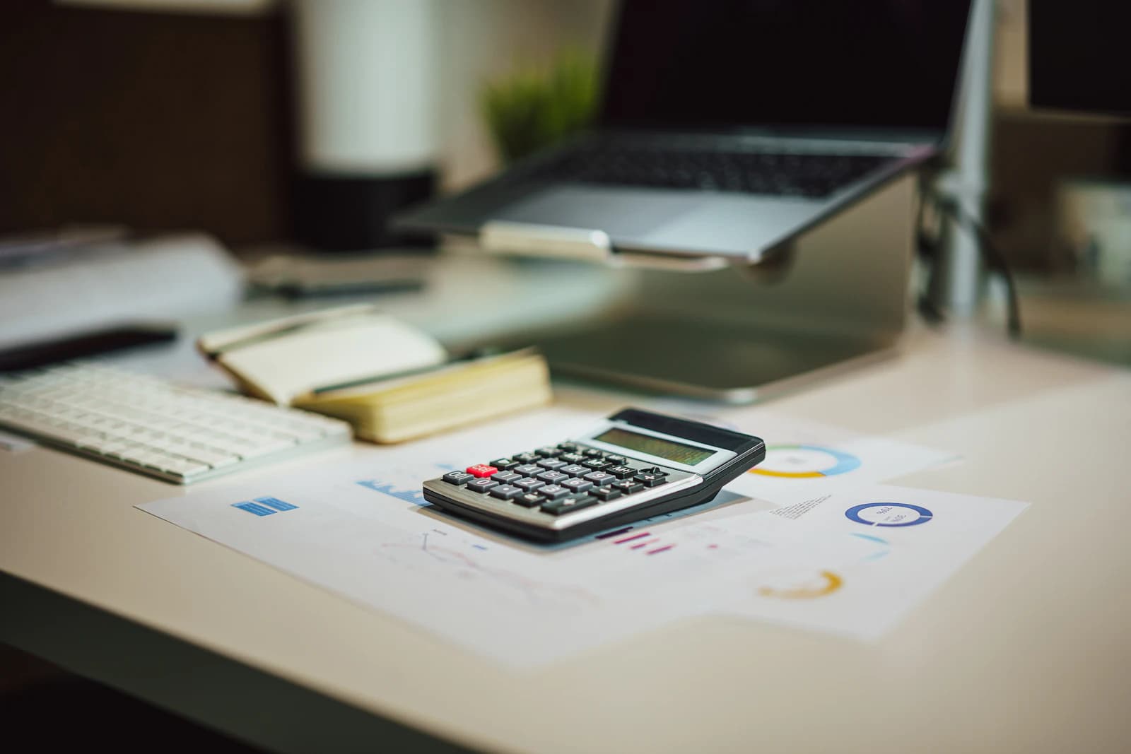 Calculadora, libreta y portátil sobre un escritorio para revisar la cifra de partida de ERPNext frente a la cuota de Holded