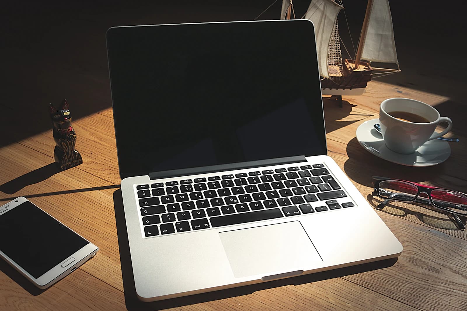 Portátil abierto, taza de café y móvil sobre una mesa de madera al sol, listos para pedir presupuesto de ERPNext