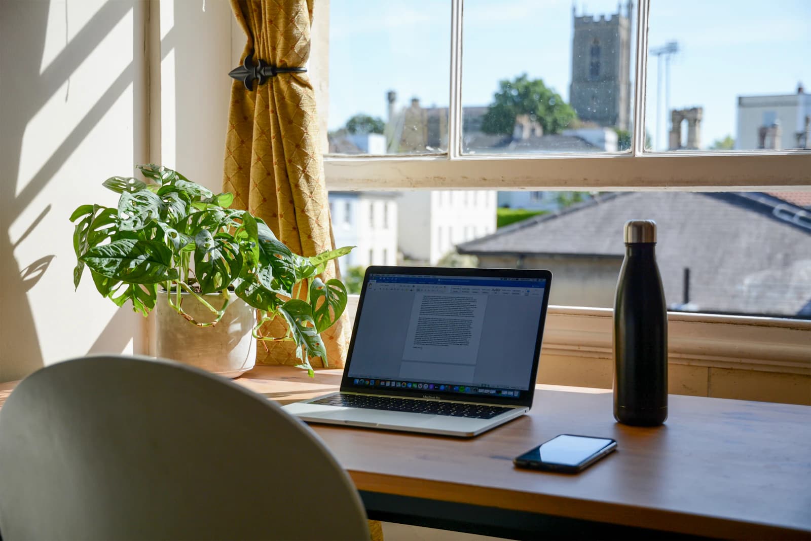 Puesto de trabajo en remoto junto a una ventana, con portátil y plantas: así trabaja un equipo digital de ERPNext sin oficinas