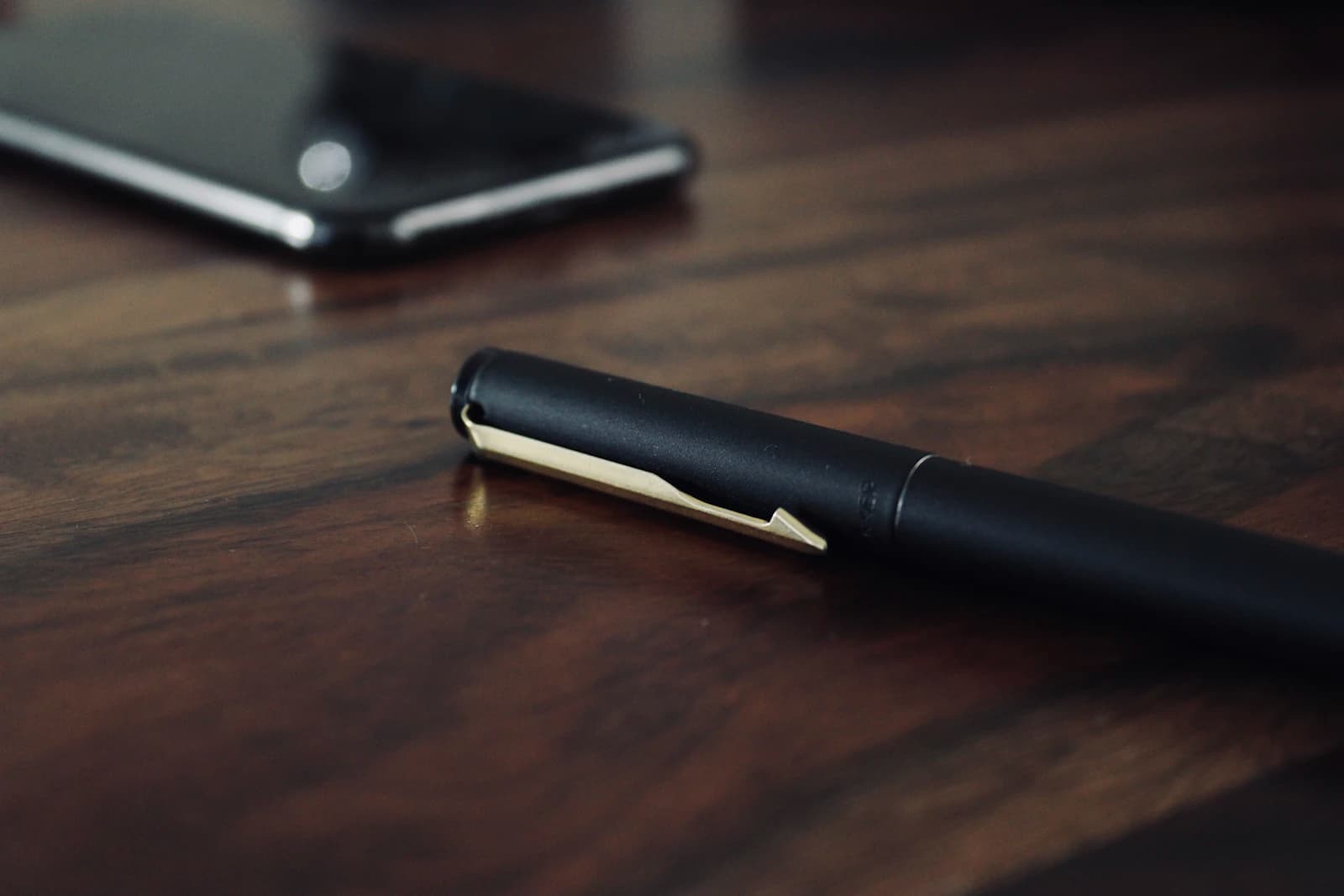 Teléfono móvil y bolígrafo sobre una mesa de madera oscura, listos para llamar a un cliente que da referencias de ERPNext