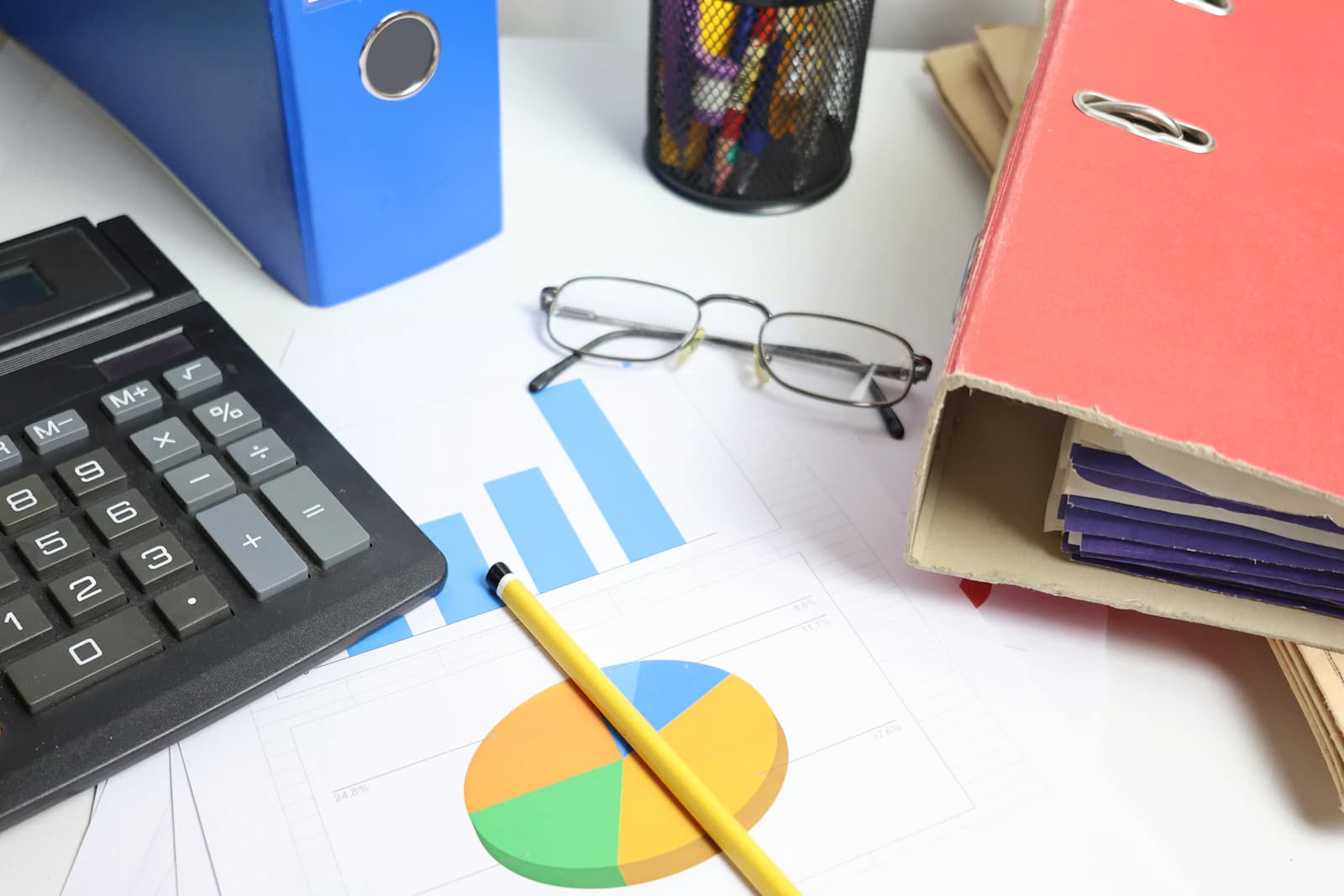 Calculadora, archivadores y gráficos impresos sobre la mesa para calcular cuánto cuesta migrar desde Oracle NetSuite