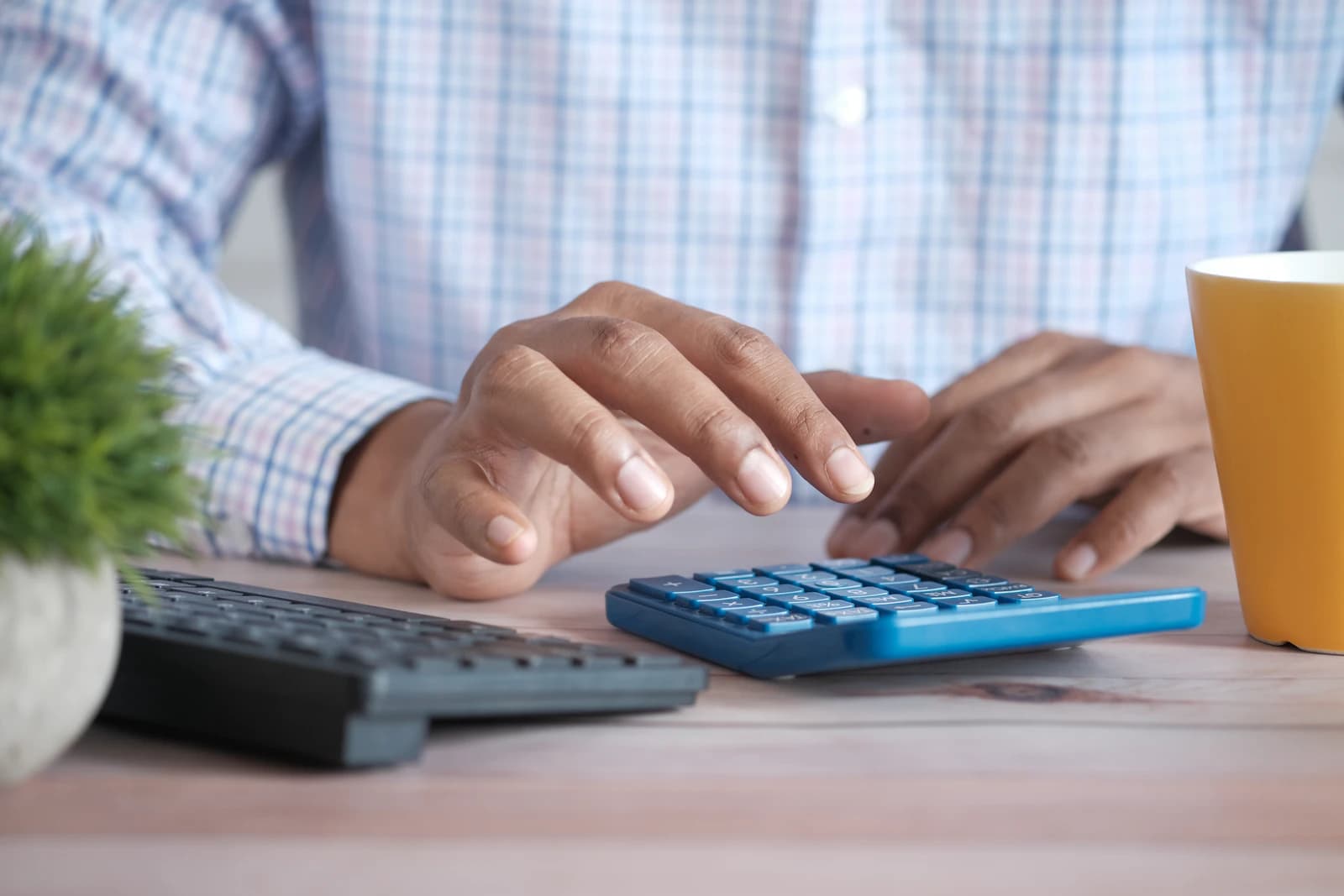 Manos con una calculadora junto al teclado y un café, calculando qué cuesta migrar de Holded a ERPNext