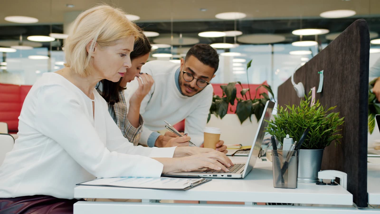 Tres compañeros revisan cifras juntos en un portátil en una oficina, valorando si dejar Oracle NetSuite por ERPNext