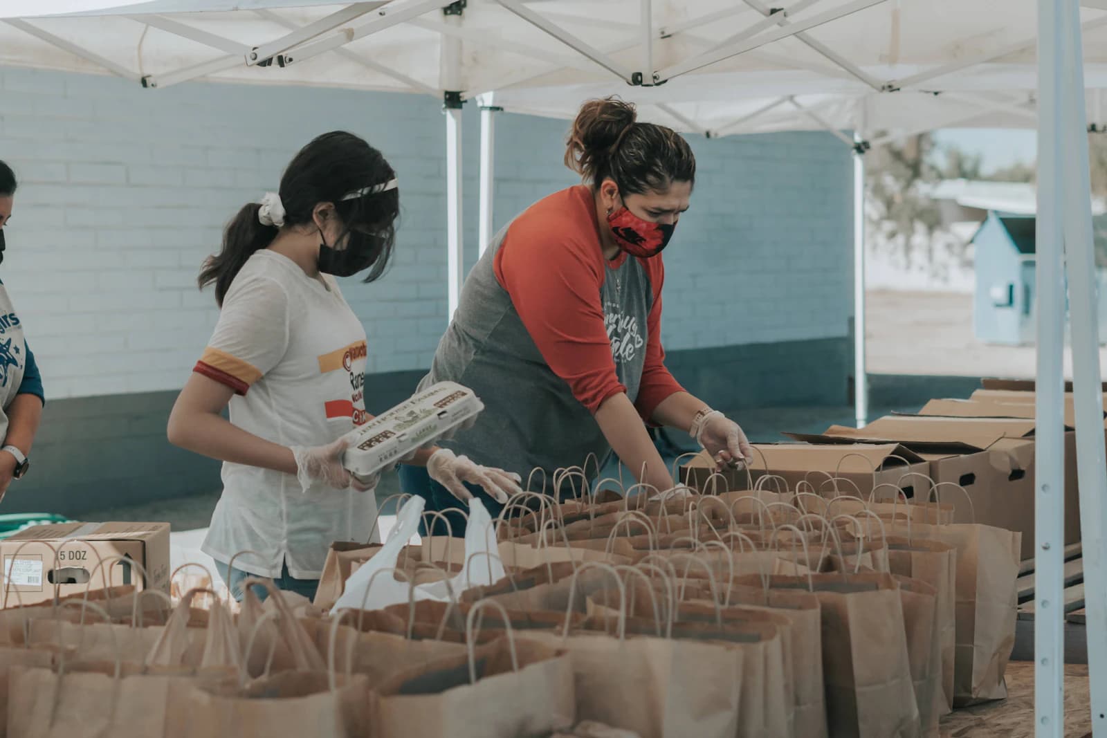 Voluntarias preparando bolsas de alimentos bajo una carpa de reparto, el trabajo diario de asociaciones, ONG y fundaciones