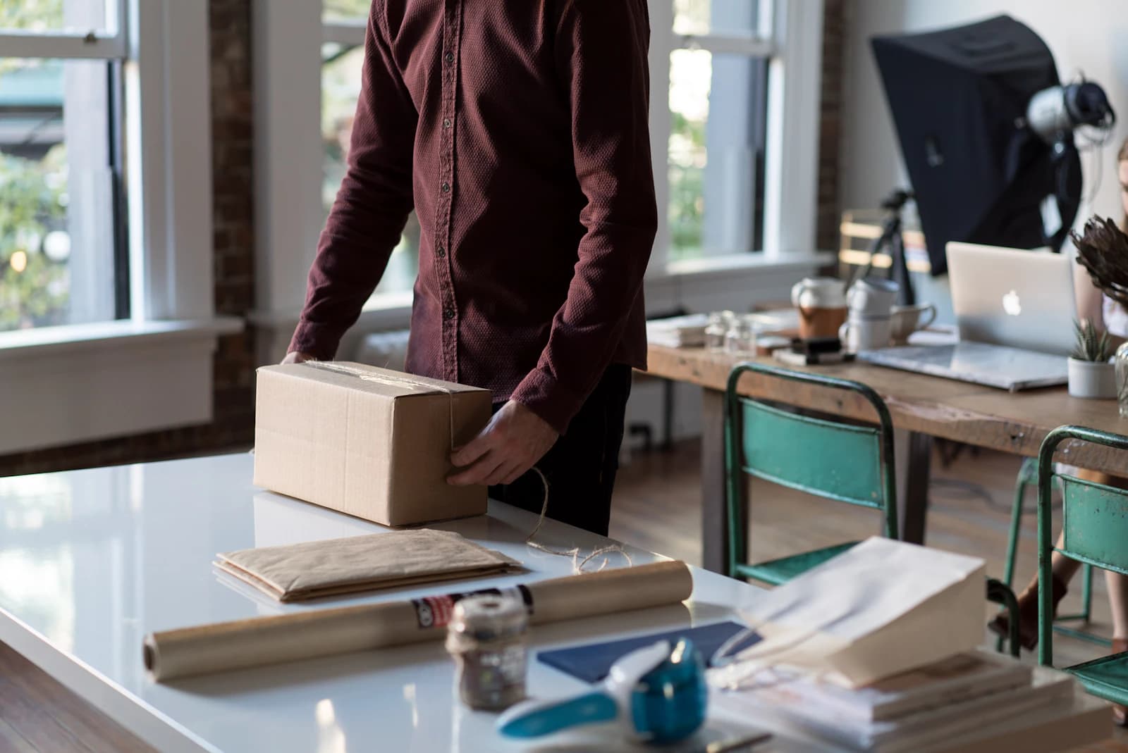 Persona cerrando una caja de cartón sobre la mesa de trabajo para preparar un pedido de una tienda online