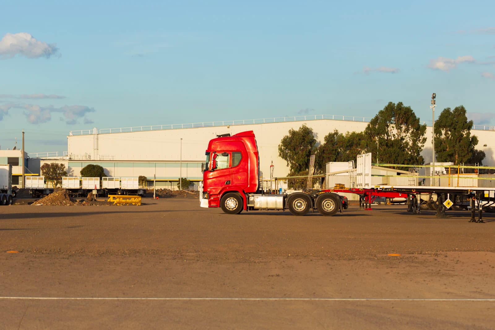 Cabeza tractora roja con semirremolque en la explanada de una nave logística, la flota que gestiona ERPNext en transporte