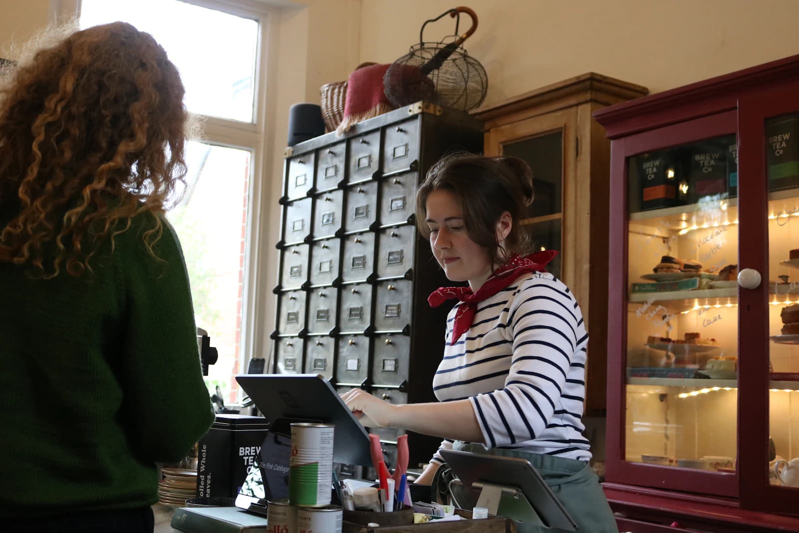 Dependienta cobrando en la caja de una tienda de té con terminal de punto de venta, un caso típico de VeriFactu en comercio